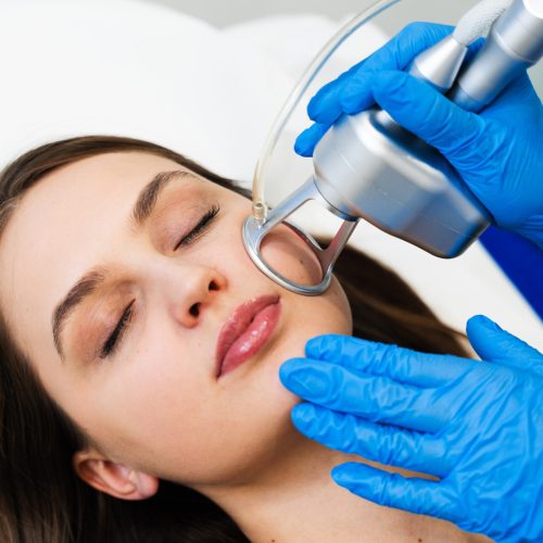Process of facial CO2 laser resurfacing. Cosmetologist removes wrinkles and scars using laser from face of attractive girl